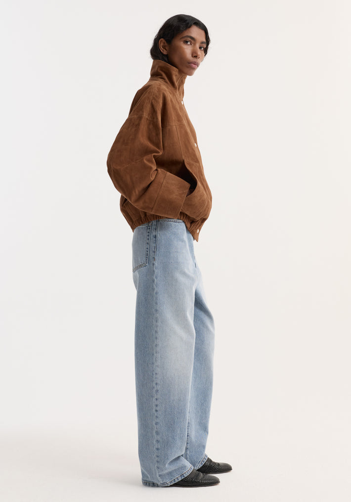 Model wearing the Reinvented suede jacket with oversized sleeves, high stand-up collar, and elasticized hem, paired with high-waisted wide-leg jeans and textured shoes.