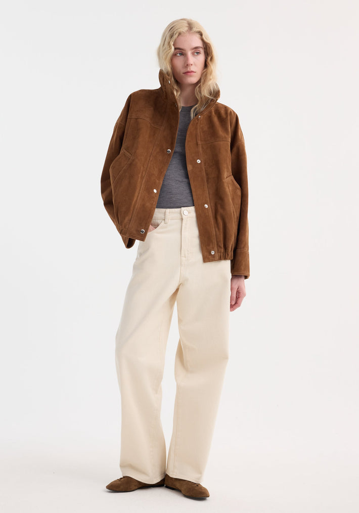 Young adult in a Reinvented suede jacket | cognac, with relaxed bomber style, stand collar, and snap buttons, paired with wide-leg jeans and suede flats.