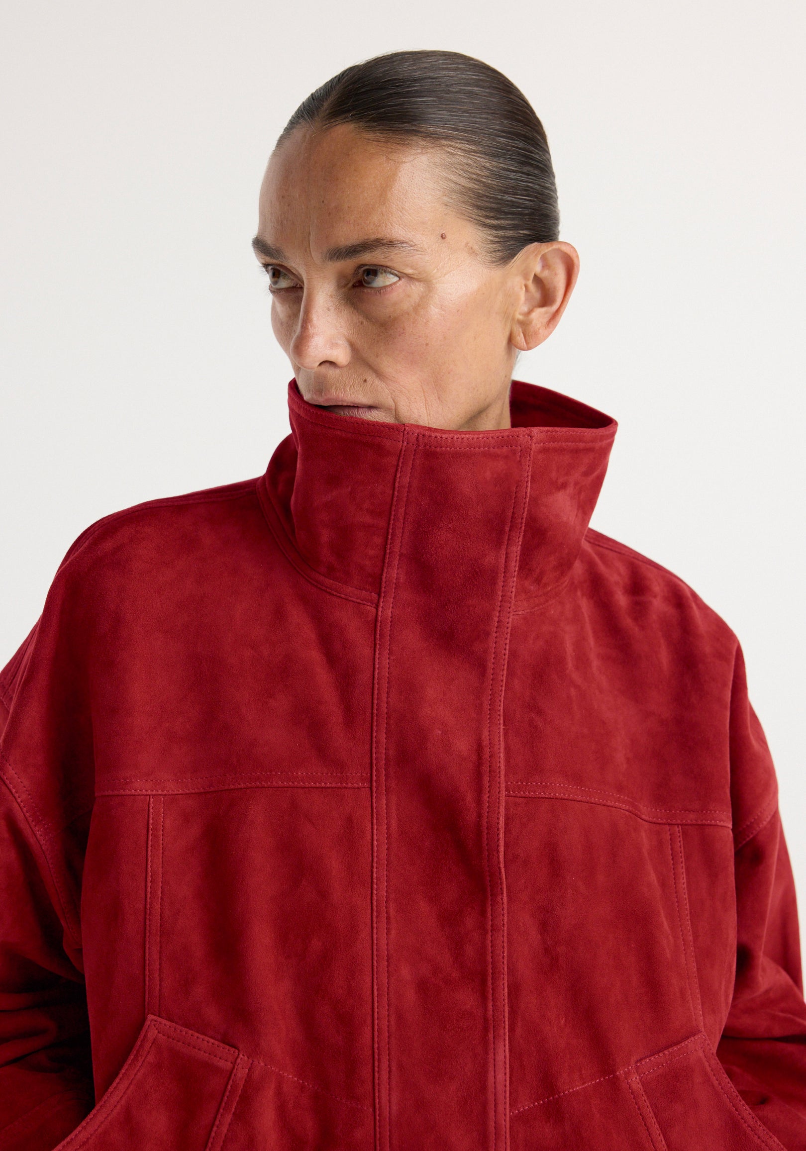 Close-up of a woman wearing a high-collar red suede jacket, showcasing the soft texture and structured design of the Reinvented suede jacket | red.
