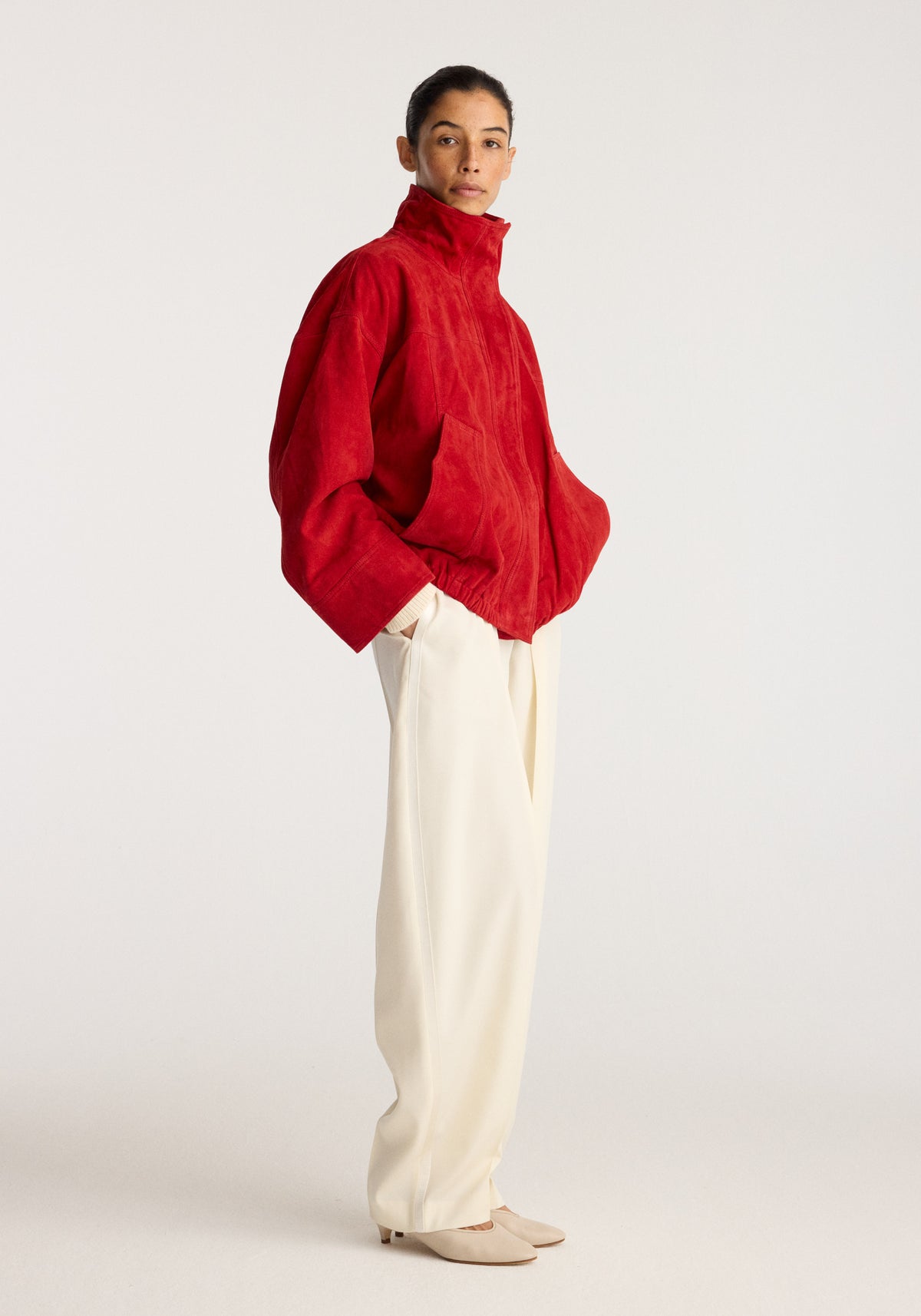 Reinvented suede jacket | red worn by a model with a high collar and long sleeves styled with cream trousers and beige flats