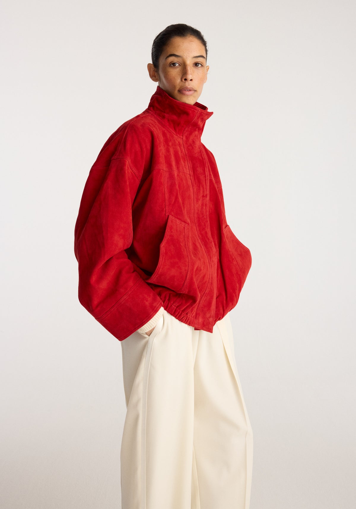 Reinvented suede jacket | red worn by a model with a high collar long sleeves and relaxed fit styled with cream trousers