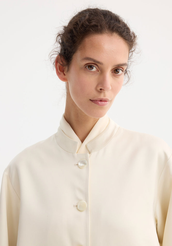 Young woman wearing cream Mandarin pearl button satin jacket, featuring a high collar and pearl buttons, showcasing the jacket's elegant design and texture.
