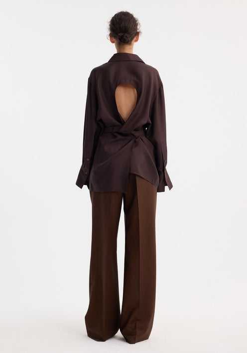 Model wearing Deconstructed silk shirt | mahogany, featuring an open back with tie detail, matched with wide-leg trousers and beige pointed-toe shoes.