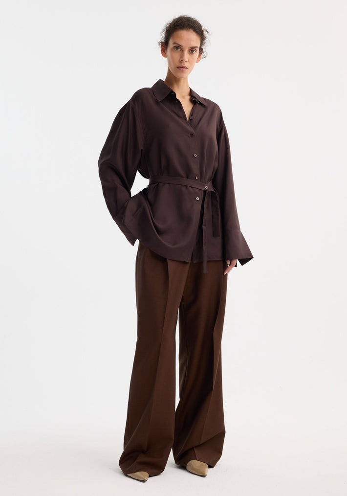 Model wearing Deconstructed silk shirt | mahogany, featuring an open back with tie detail, matched with wide-leg trousers and beige pointed-toe shoes.