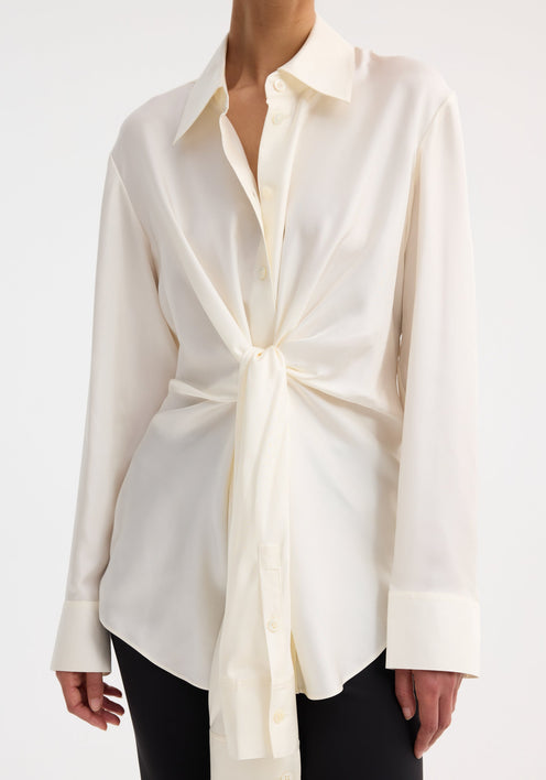 Silk knotted shirt | cream, worn by a model, features a twisted tie front design, paired with black trousers and strappy sandals.