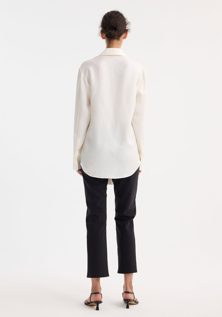 Silk knotted shirt in cream, rear view: features a twisted tie front design, worn with black cropped trousers and sandals, model's hair in a loose bun.