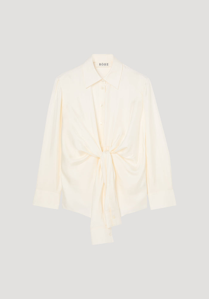 Silk knotted shirt | cream: Cream-colored, long-sleeve blouse with a pointed collar, featuring a unique twisted knot design at the waist for a draped effect.