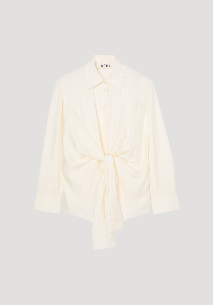 Silk knotted shirt | cream: Cream-colored, long-sleeve blouse with a pointed collar, featuring a unique twisted knot design at the waist for a draped effect.