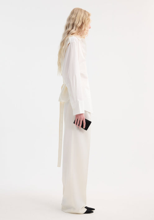 Person wearing Poplin silk combined gilet-shirt in optic white, featuring a crisp cotton front and silk back, paired with wide-leg trousers and holding a black clutch.