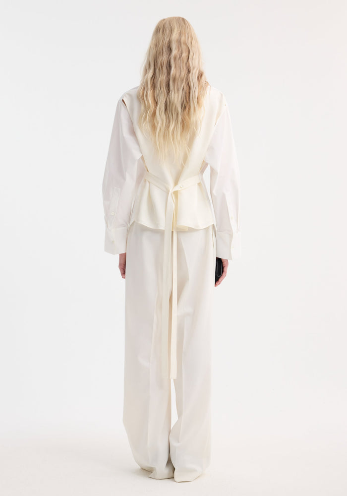 Model in Poplin silk combined gilet-shirt, featuring a long-sleeved button-down and sleeveless wrap vest with wide-leg trousers, viewed from the back.