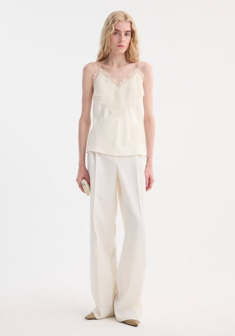 Tall person models Lace camisole | cream with v-neck, lace trim, and adjustable straps, paired with high-waisted trousers, showcasing minimalist elegance.