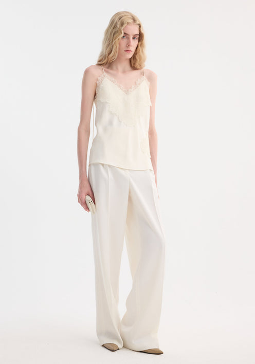 Tall person models Lace camisole | cream with v-neck, lace trim, and adjustable straps, paired with high-waisted trousers, showcasing minimalist elegance.