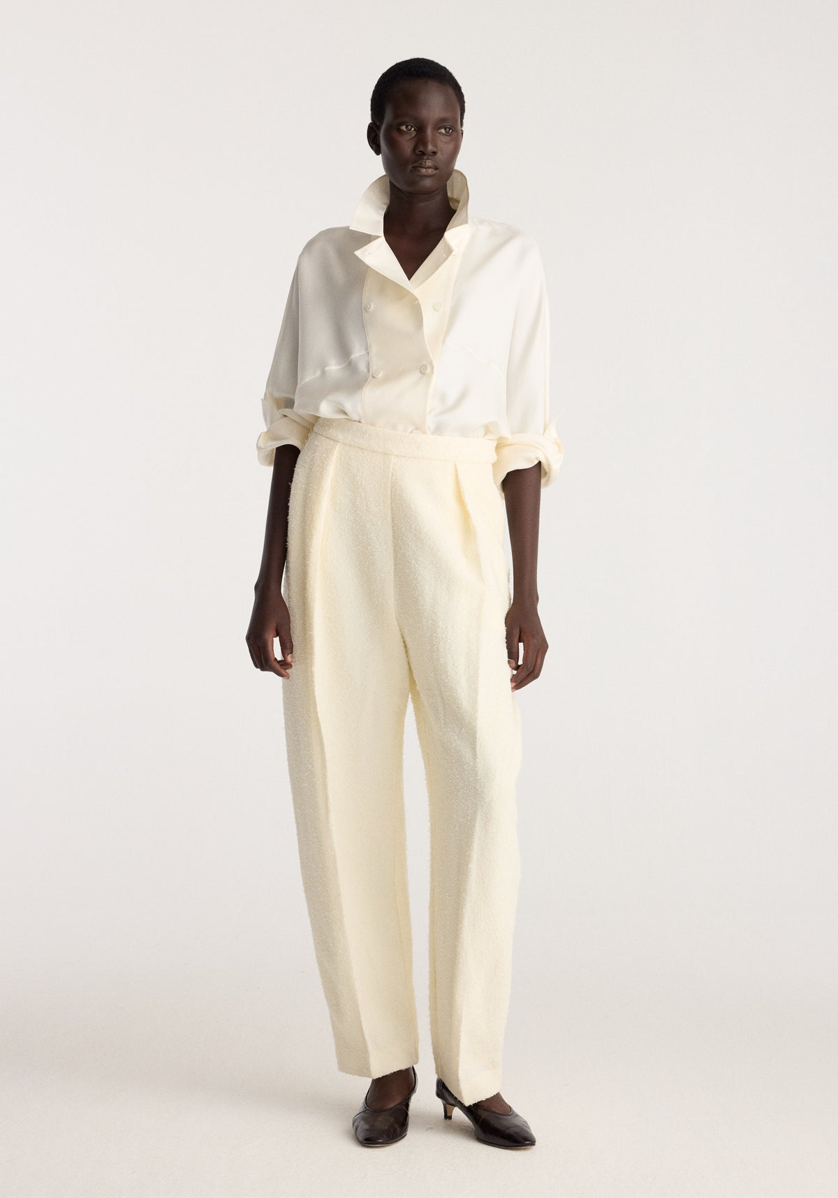 Double breasted silk top | cream worn by a model with rolled sleeves and pointed collar paired with cream trousers and black shoes