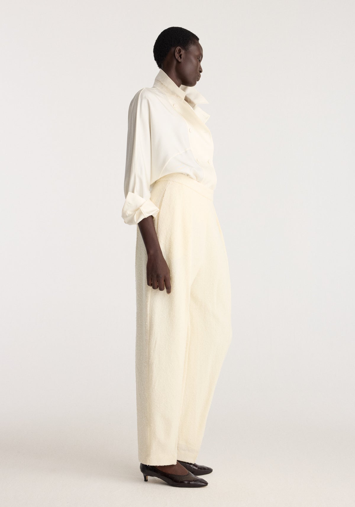 Puck - Sculptural bouclé tailored trousers | cream shown on a model in profile with a cream shirt and dark pointed shoes