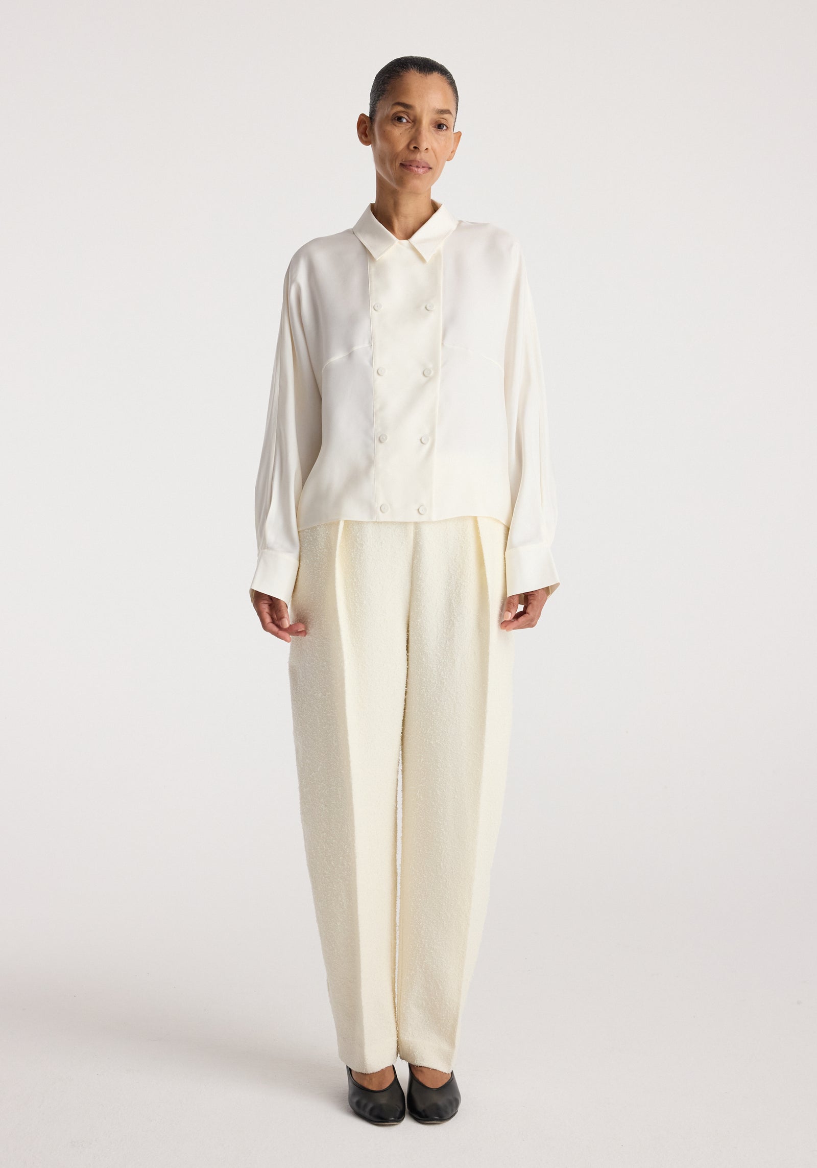 Model wearing Double breasted silk top | cream, a cream long sleeve button front top with pointed collar and relaxed fit styled with wide leg trousers.