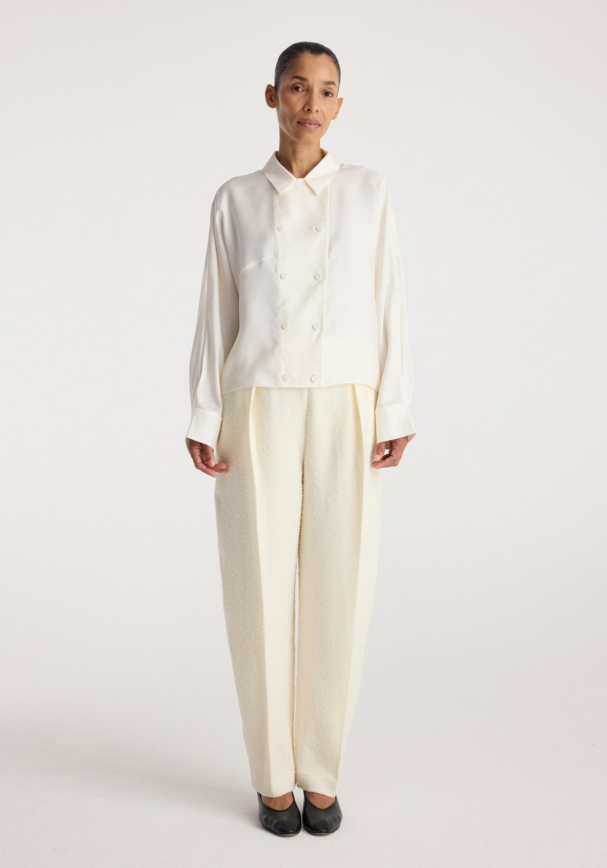 Model wearing Double breasted silk top | cream, a cream long sleeve button front top with pointed collar and relaxed fit styled with wide leg trousers.