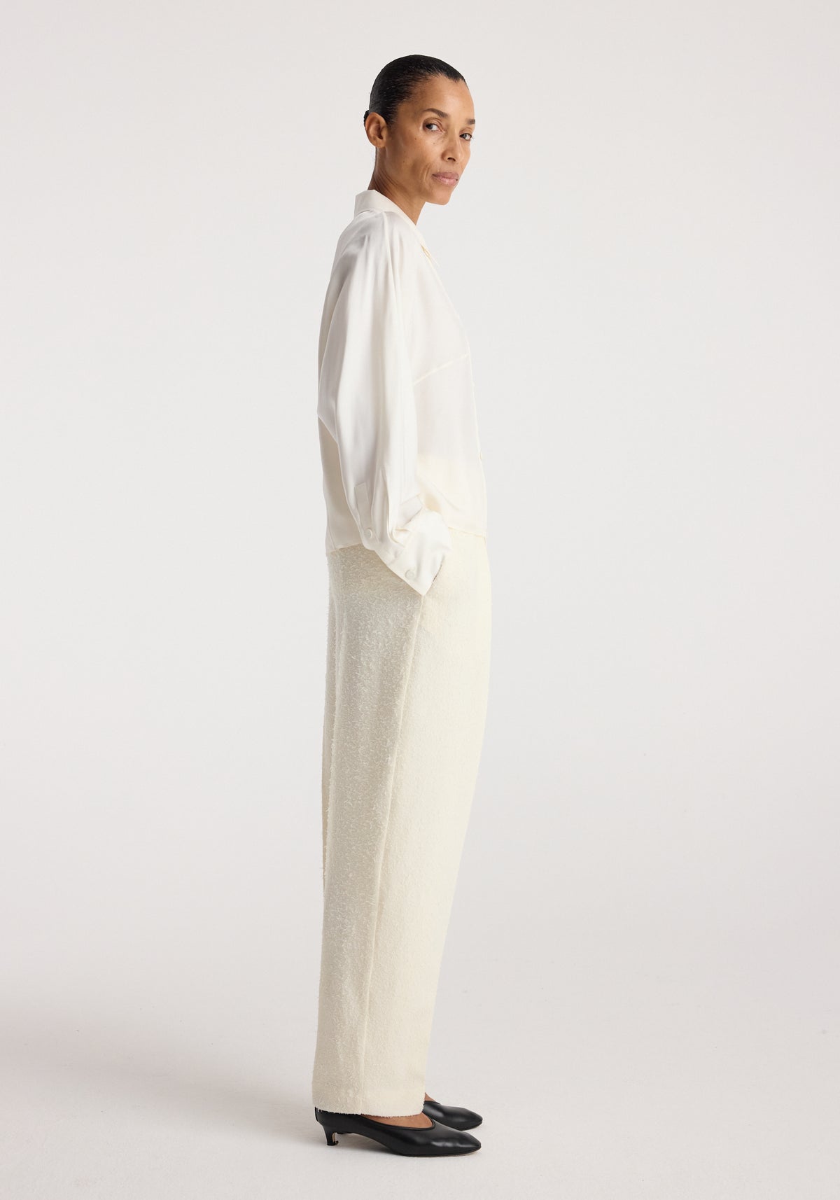 Model wearing Double breasted silk top | cream with cream trousers and black flats, shown in profile against a neutral studio background