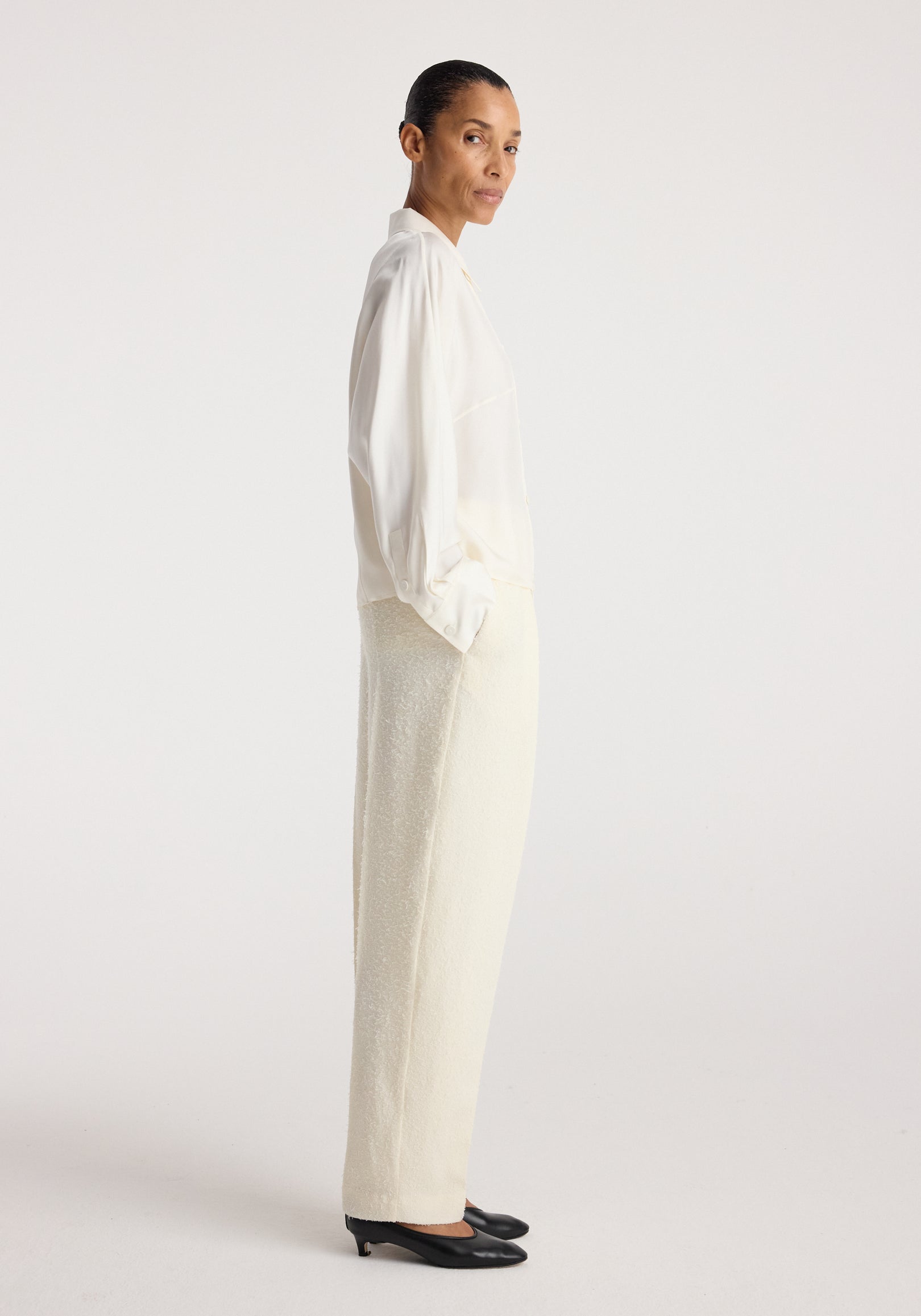 Model wearing Double breasted silk top | cream with cream trousers and black flats, shown in profile against a neutral studio background