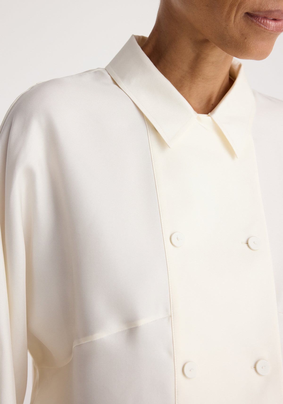 Double breasted silk top | cream shown in close-up on a model, featuring a pointed collar, long sleeves, and a double row of covered buttons.