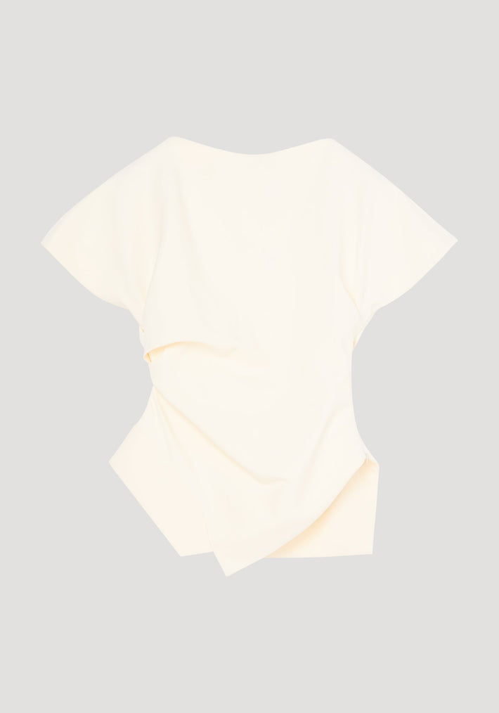 Draped lapel top in off-white with sculptural asymmetrical silhouette; features wide sleeves, scooped neckline, and overlapping fabric panels for a modern, architectural look.