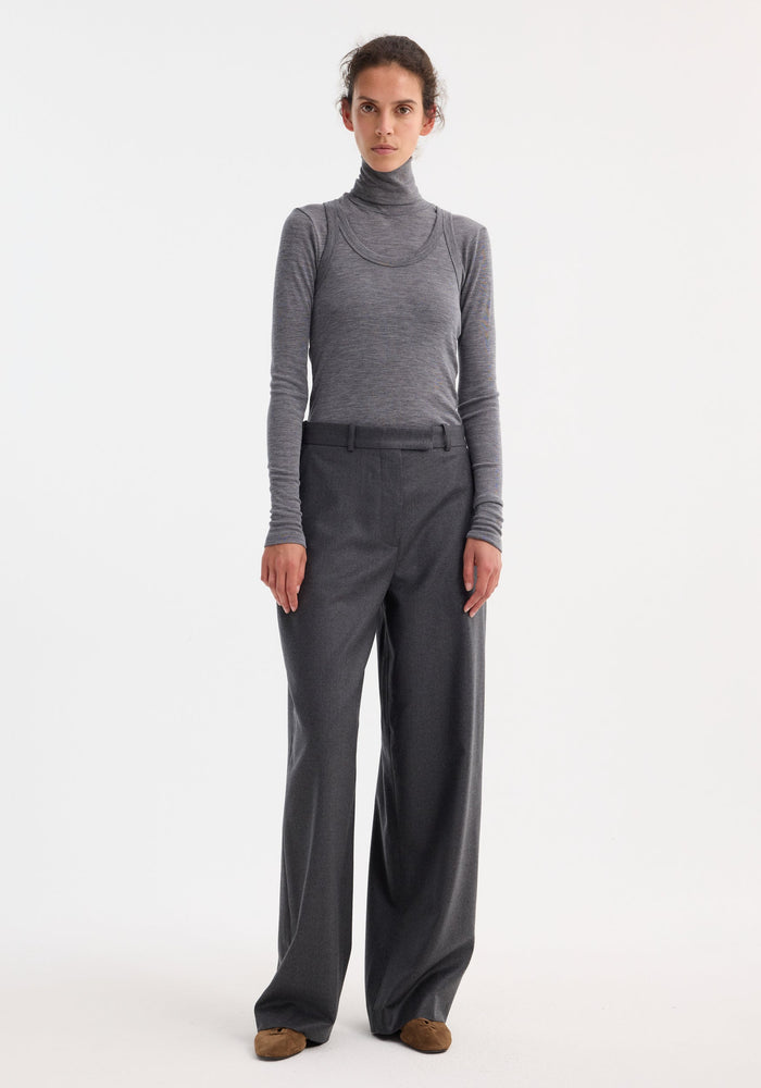Woman wearing Double-layer wool top in mid grey melange, featuring a fitted turtleneck and tank, paired with wide-leg trousers and brown suede flats.