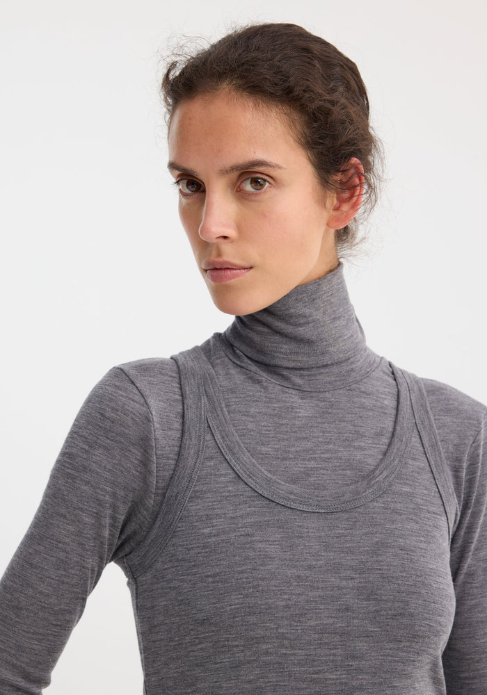 Young woman wearing a Double-layer wool top | mid grey melange, featuring a fitted turtleneck and tank in soft merino jersey, posed against a light background.