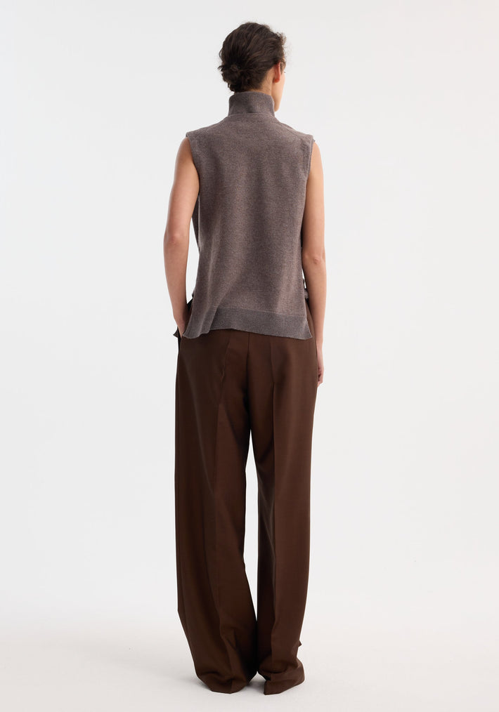 Model wearing Double-layered knit top | mud melange, showcasing a deconstructed design with tie-sleeve details and a wide-leg trouser ensemble against a plain backdrop.