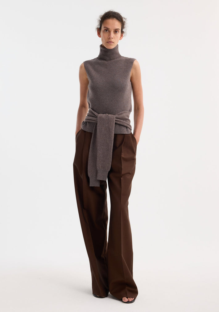 Model wearing the Double-layered knit top in mud melange, featuring a fitted turtleneck underlayer, tie-sleeve detailing, and a knit sweater tied at the waist.