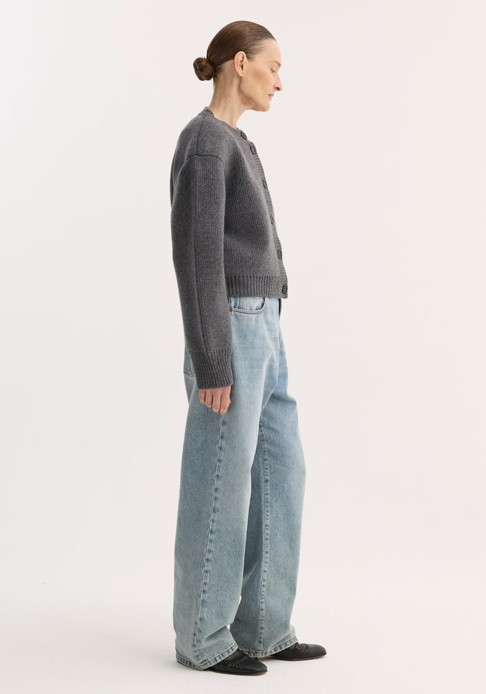 Side-profile of a model wearing the Statement Shoulder Cardigan in mid grey melange, featuring a button front and structured shoulders, paired with wide-leg jeans.