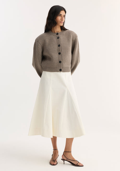 Woman wearing the Statement Shoulder Cardigan in clay melange, showcasing its chunky knit, oversized fit, and large dark buttons, paired with a high-waisted midi skirt.