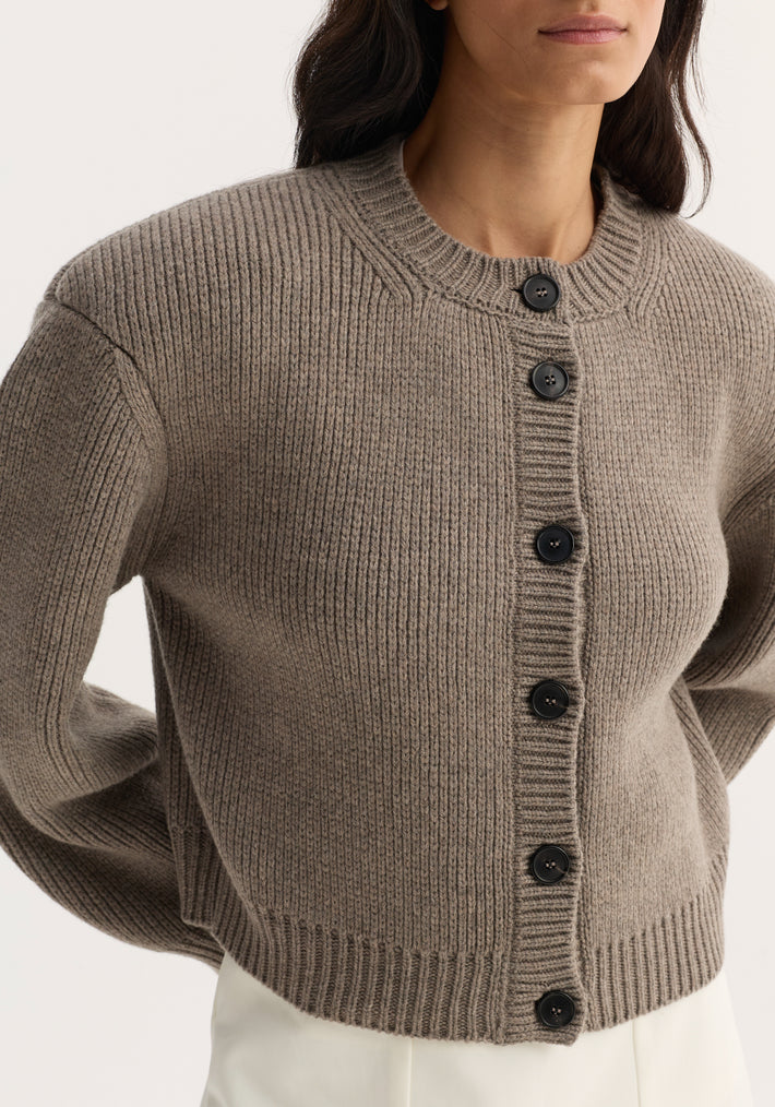 Person wearing the Statement Shoulder Cardigan in clay melange, featuring chunky rib-knit, oversized fit, structured shoulders, and five large dark buttons.