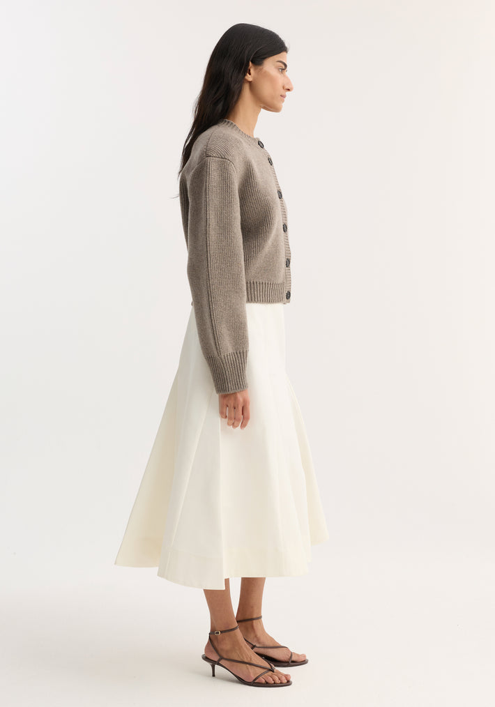 Model wearing Statement Shoulder Cardigan | Clay Melange, showcasing its oversized fit and structured shoulders, paired with a cream midi skirt and dark strappy sandals.