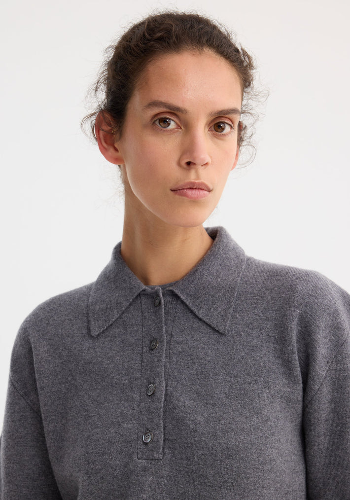 Young woman wearing a grey Compact knitted polo with a pointed collar, long sleeves, and a 3-button front, crafted from a wool-cashmere blend.
