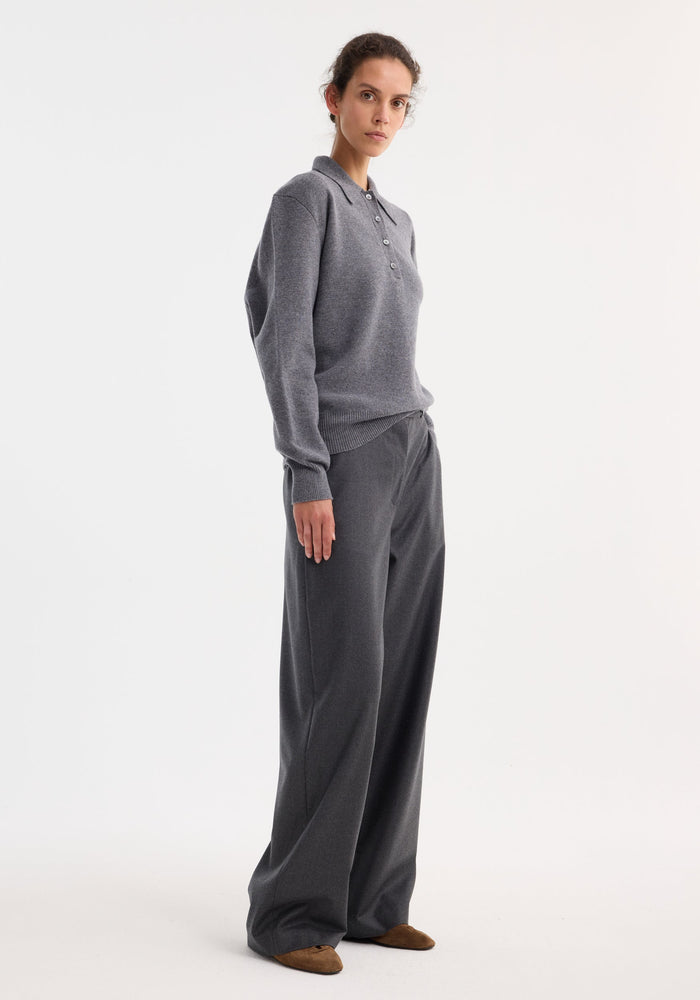 Woman wearing Compact knitted polo in mid grey melange with a relaxed fit, paired with matching wide-leg trousers and brown suede flats, showcasing a minimalist style.