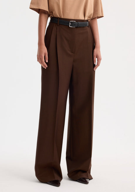 Model wearing Mid-waist tailored trousers in mahogany, featuring high-waisted, wide-leg fit with double pleats, styled with a beige T-shirt and black belt.