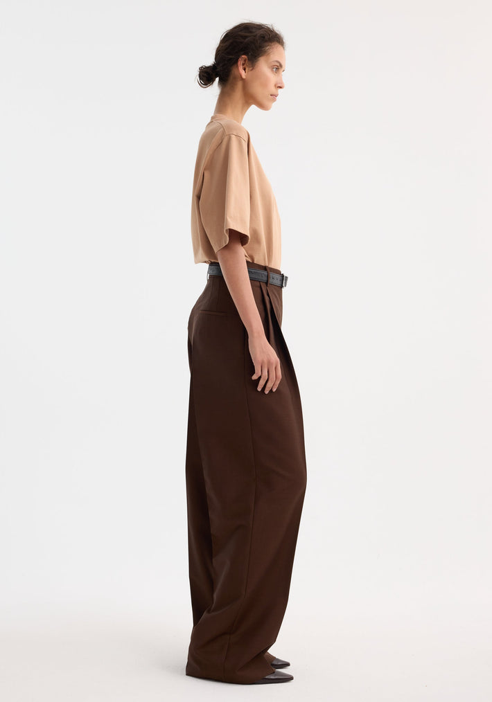 Side-profile of person in Mid-waist tailored trousers | mahogany, featuring a wide-leg, double pleats, and tailored waistband, styled with a beige T-shirt.