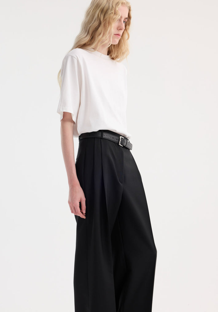 Model in Oversized cotton t-shirt, optic white, tucked into high-waisted black trousers. Features include a relaxed fit, drop shoulder, and crew neck.
