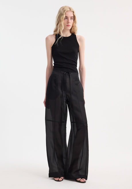 Model wearing Organza silk parachute trousers in black, featuring wide-leg design and drawstring waist, paired with a fitted sleeveless tank top and sandals.