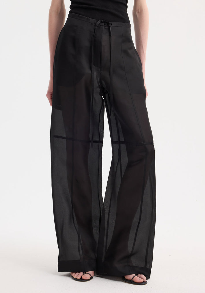 Organza silk parachute trousers in sheer black, featuring a wide-leg silhouette, drawstring waist, and semi-transparent fabric revealing a black underlayer.