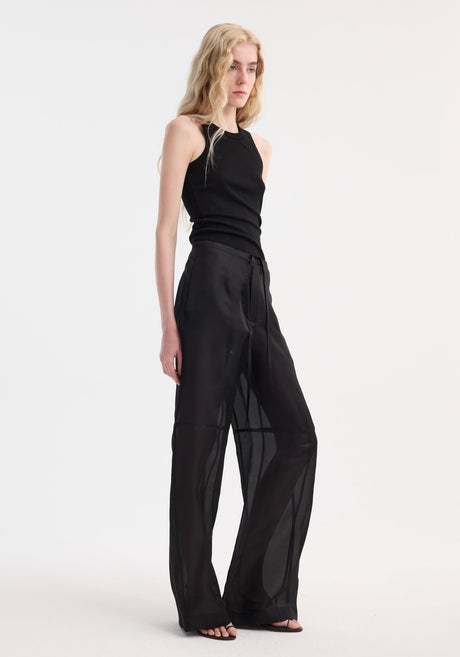 Model wearing Organza silk parachute trousers in black, featuring wide-leg design and drawstring waist, paired with a fitted sleeveless tank top and sandals.