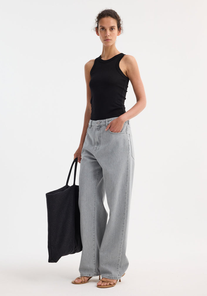 Tall woman models Signature baggy fit denim in washed grey, featuring a wide leg and low-waist fit, paired with a black tank and tote.