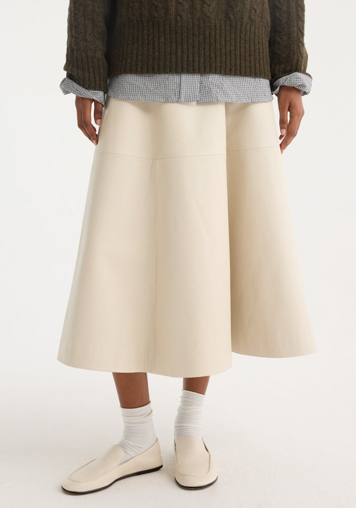 A-line leather skirt in chalk, featuring croco embossing and minimalist detailing, paired with ivory loafers and slouchy socks, highlighting its voluminous silhouette.
