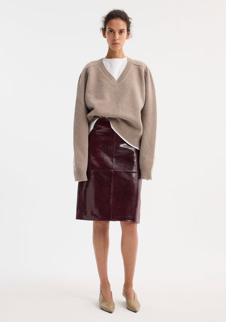 Model wearing a Snake leather skirt | burgundy snake, featuring a glossy, high-waisted design with subtle snake-skin texture, paired with a beige sweater and taupe mules.