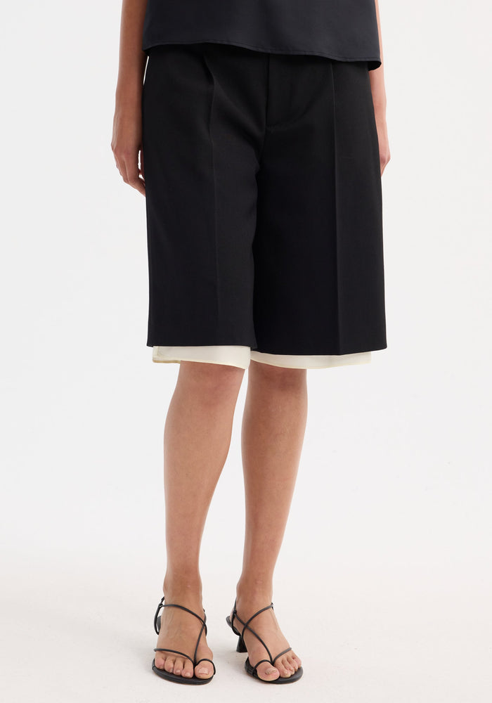 Contrast extended lining shorts in black with wide legs, tailored waistband, and visible white underlayer, paired with black strappy heeled sandals.