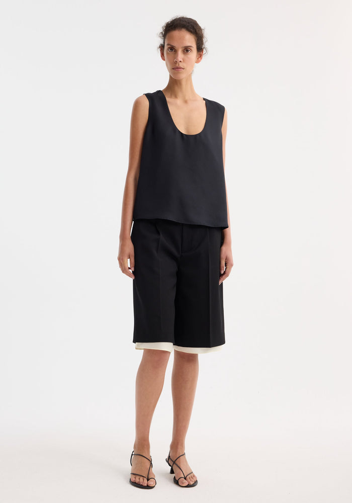 Model wearing Contrast extended lining shorts, showcasing tailored culottes with sharp pleats and visible white underlayer, paired with a loose sleeveless top and strappy heels.