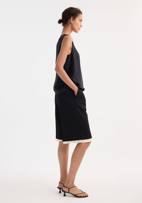Model wearing Contrast extended lining shorts, showcasing tailored culottes with sharp pleats and visible white underlayer, paired with a loose sleeveless top and strappy heels.