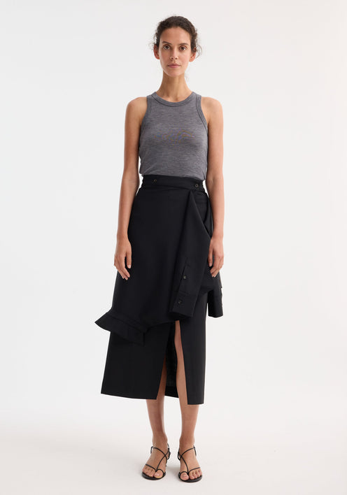 Person wearing a Shirt wrap skirt in black, featuring an asymmetrical wrap, front slit, and deconstructed sleeves, paired with a heather-gray tank top and black sandals.