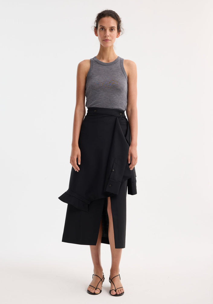 Person wearing a Shirt wrap skirt in black, featuring an asymmetrical wrap, front slit, and deconstructed sleeves, paired with a heather-gray tank top and black sandals.