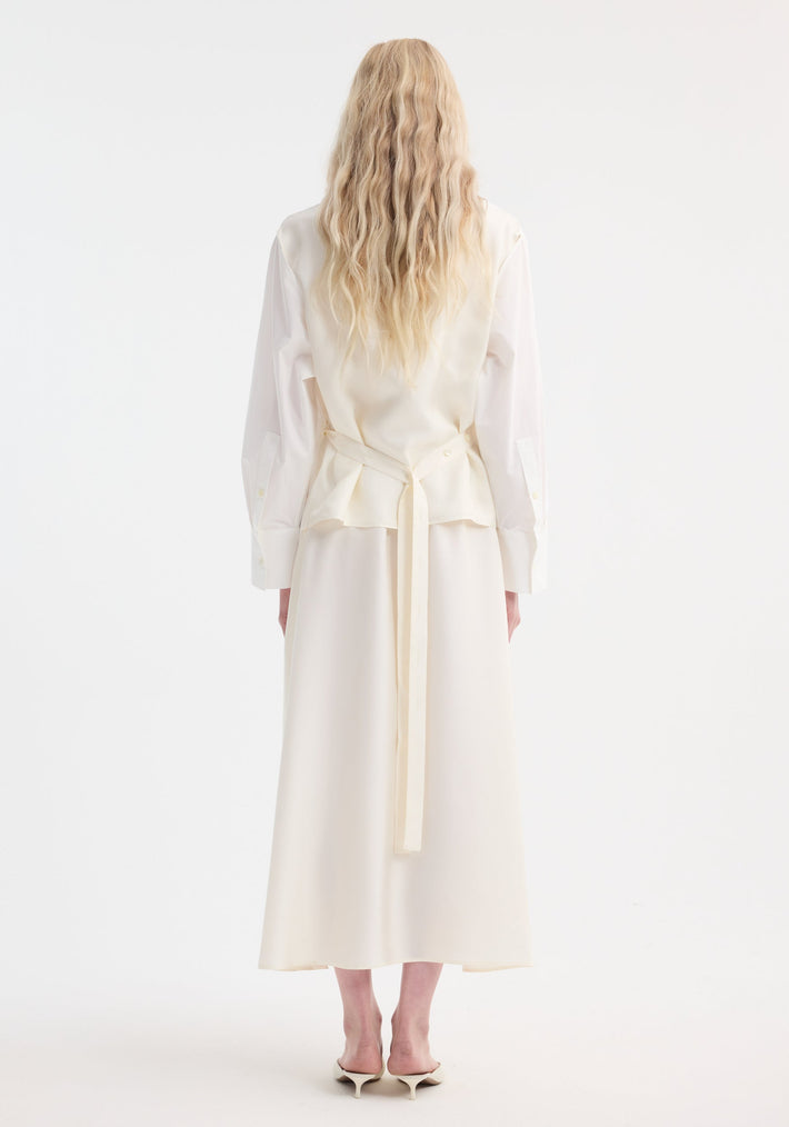 Back view of a person in a Poplin silk combined gilet-dress featuring a deconstructed design with open armholes and a flowing ankle-length silhouette.