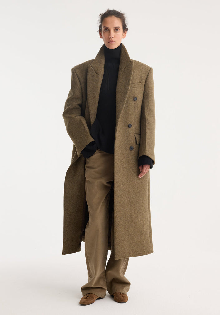 Hourglass wool coat in forest melange, featuring a double-breasted design, notched lapels, broad shoulders, and flap pockets, paired with a black turtleneck and tan trousers.